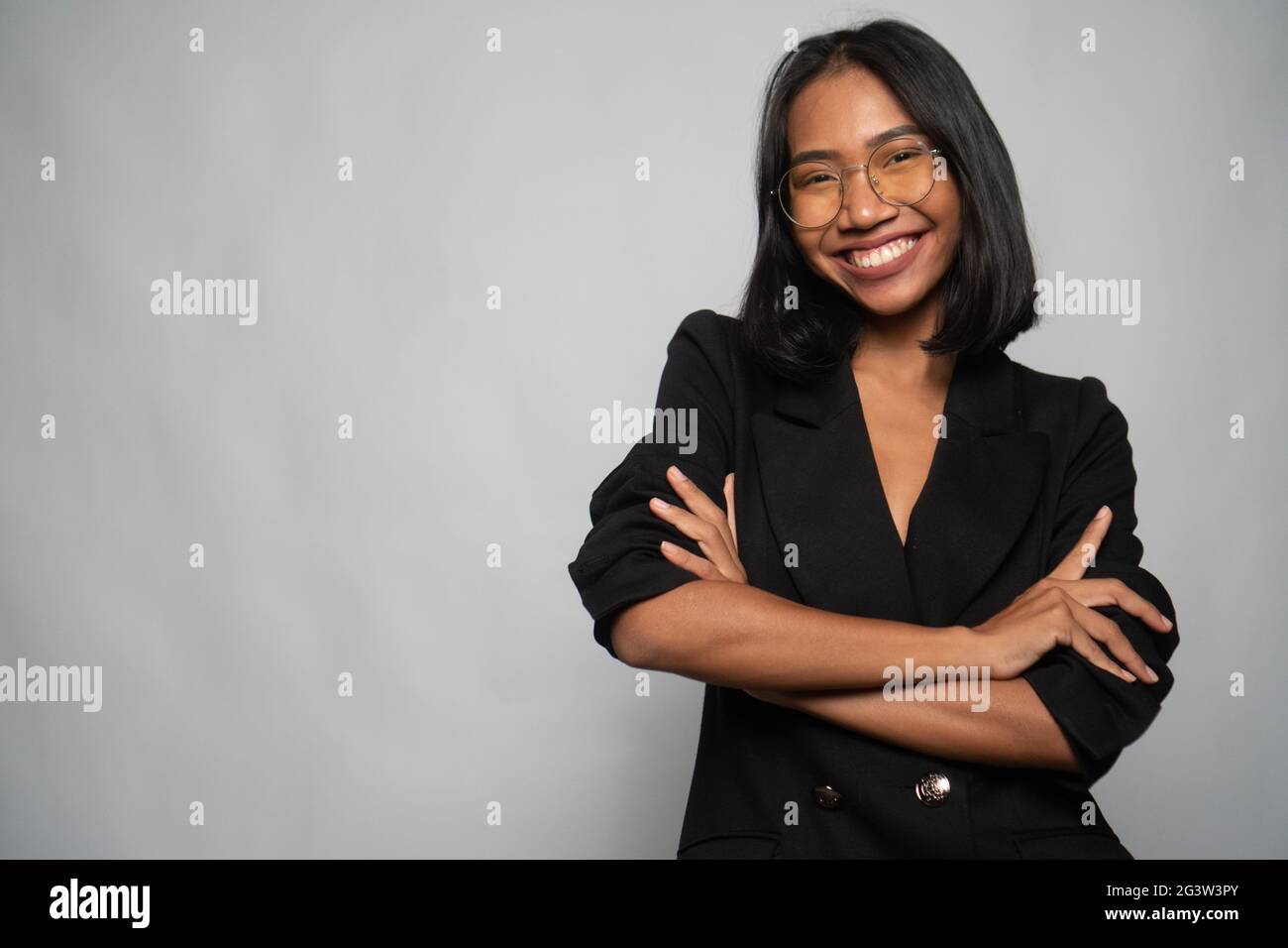 Attraente giovane donna asiatica in elegante blazer nero e vetri isolati su parete grigio chiaro Foto Stock