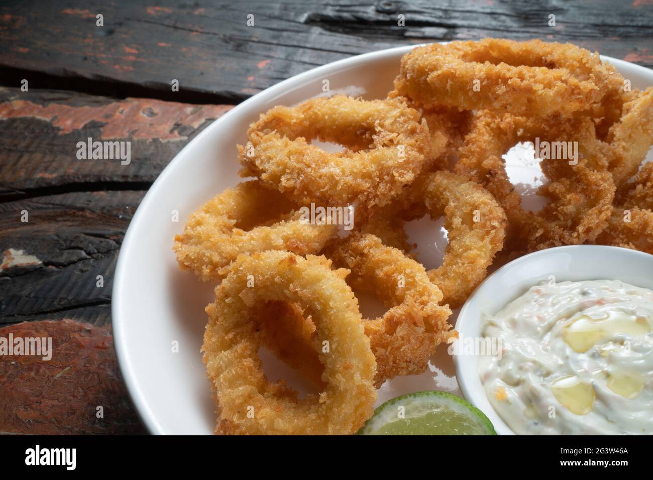 Anelli di calamari fritti con salsa a tuffo su tavolo rustico in legno Foto Stock