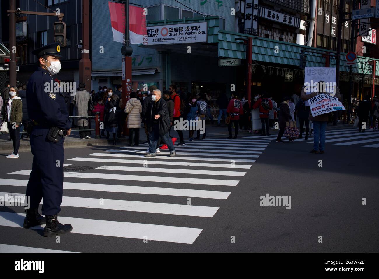 Maschio giapponese che detiene Covid Conspiracy e anti covid-19 poster vaccino lungo via Kaminarimon-Dori, Asakusa, mentre un ufficiale di polizia guarda sopra Foto Stock