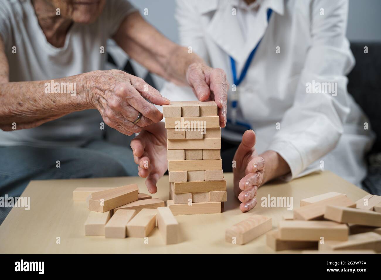Jenga gioco. Il tema è la demenza, l'invecchiamento e i giochi per gli anziani. Caucasica anziana costruisce torre di blocchi di legno con il hel Foto Stock