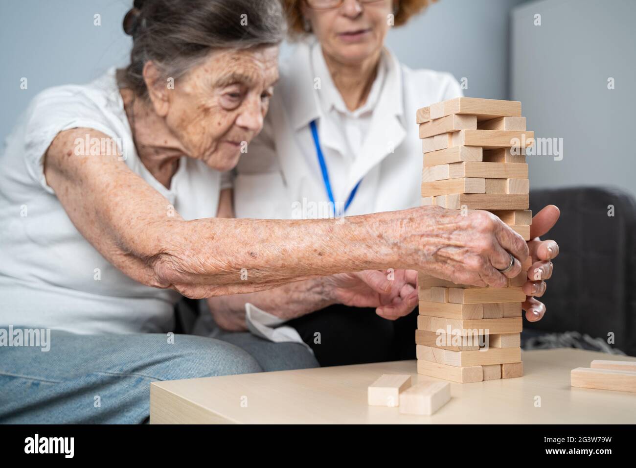 La terapia della demenza in modo giocoso, addestrando le dita e le abilità motorie fini, costruisce i blocchi di legno nella torre, giocando Jenga. Senior w Foto Stock