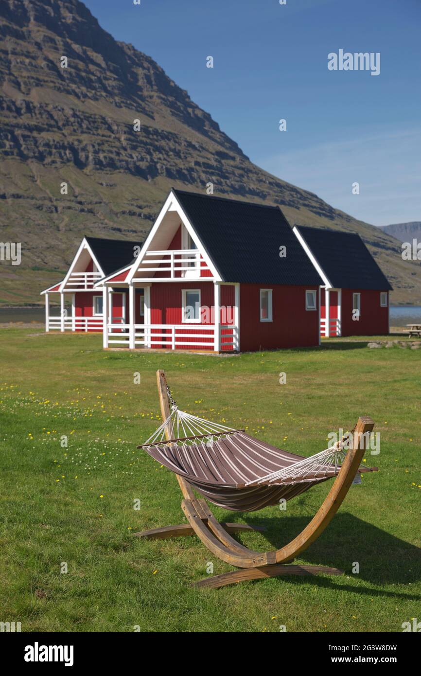 Casa tradizionale con pannelli in legno dipinto di rosso con la possente montagna di Holmatindur a Eskifjordur, Islanda Foto Stock
