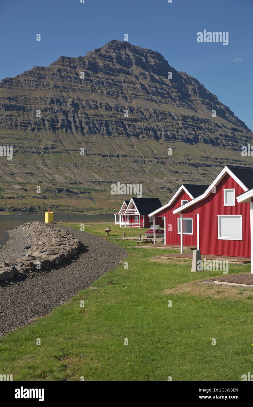 Casa tradizionale con pannelli in legno dipinto di rosso con la possente montagna di Holmatindur a Eskifjordur, Islanda Foto Stock