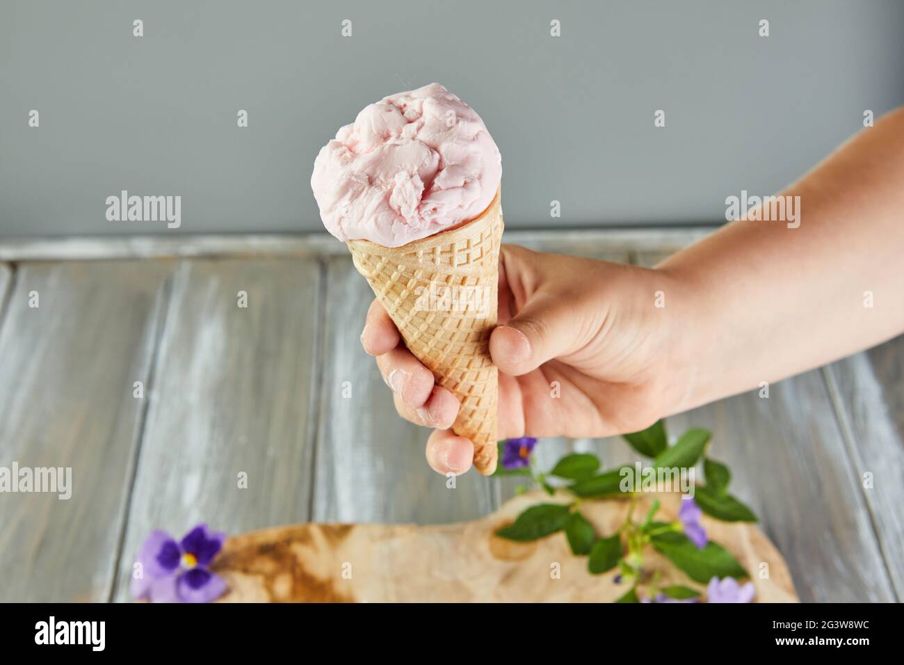Cono per waffle con gelato su sfondo grigio con fiori. Foto Stock