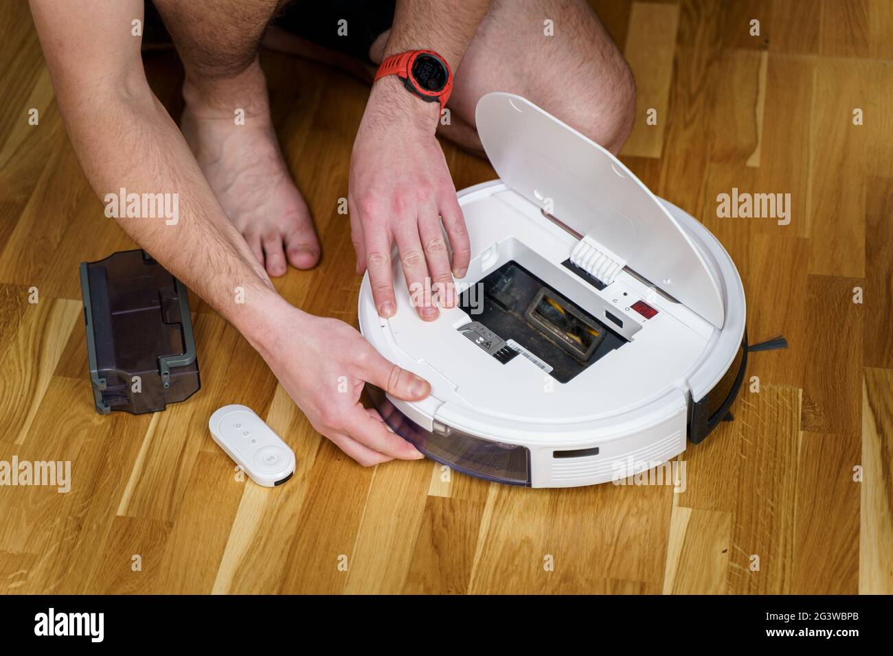 Concetto di casalinghi e tecnologia. Manutenzione ed assistenza di aspirapolvere robot. Pulizia, riparazione, sostituzione delle parti. Man r Foto Stock