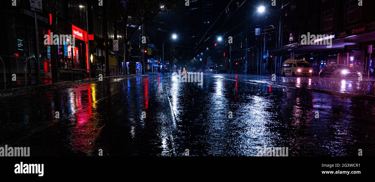 Una vuota strada cittadina piovosa di notte con luci che si riflettono in pozzanghere a Melbourne Foto Stock
