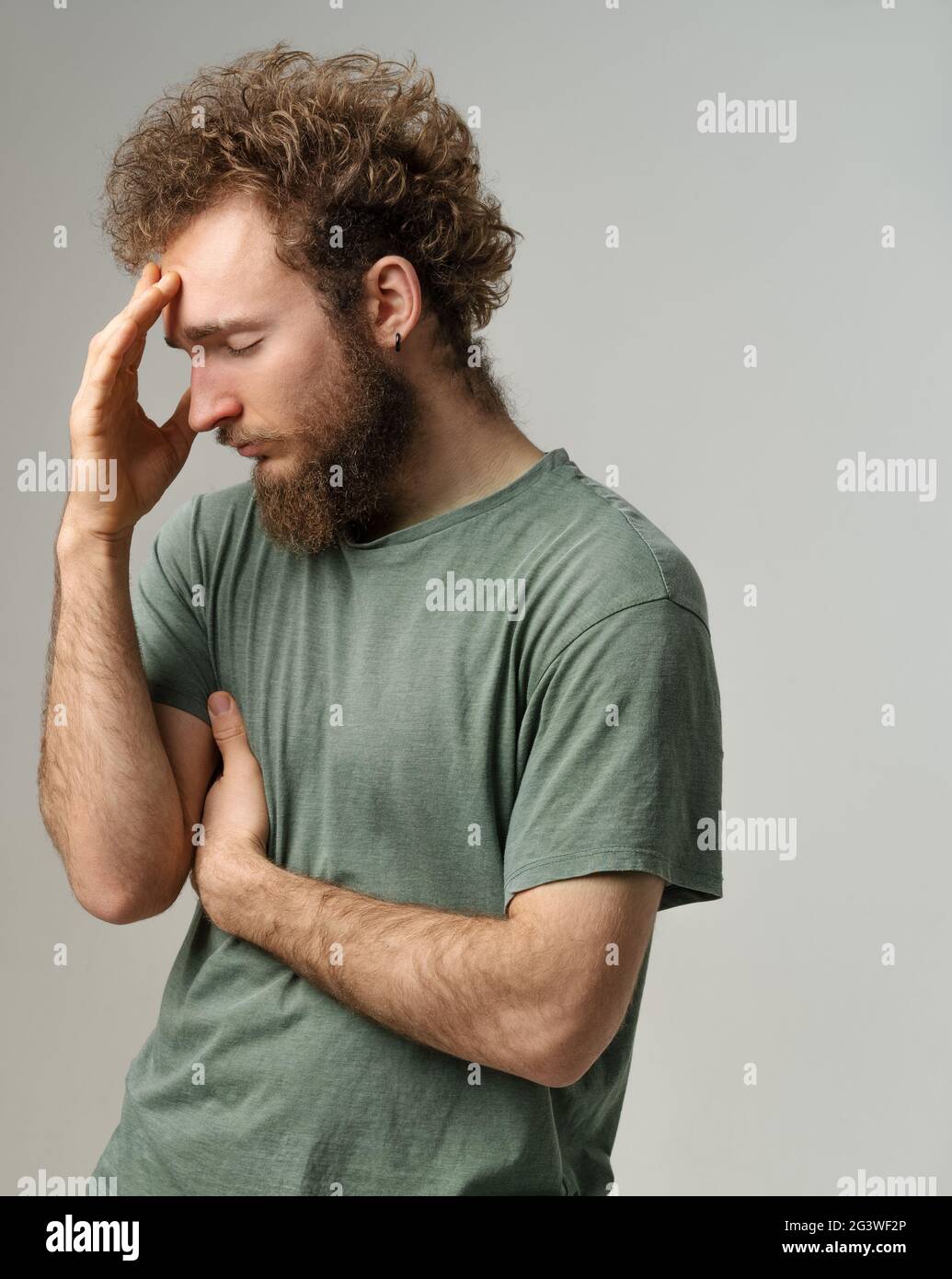 Ha mal di testa o vergogna per un giovane avversario che tocca la fronte. Bel giovane con capelli ricci in t-shirt oliva iso Foto Stock