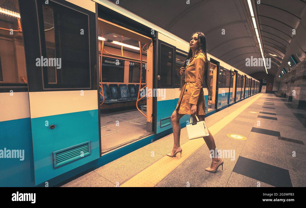 Camminando dentro ad una porta aperta di un treno della metropolitana vuoto bella ragazza giovane con le gambe lunghe belle in un cappotto di molla giallo e un Foto Stock