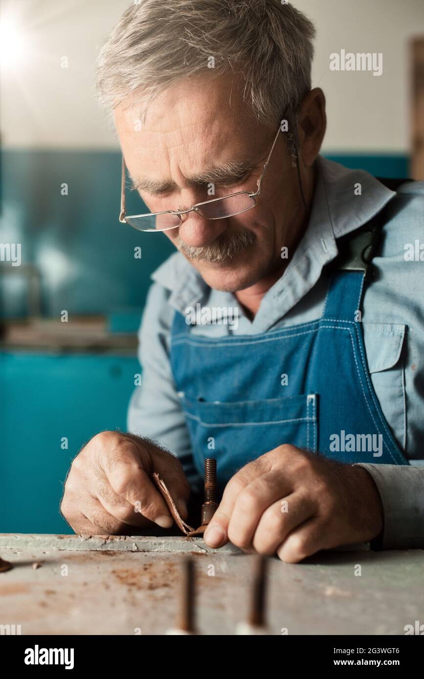 Un vecchio maestro con gli occhiali lavora in un'officina Foto Stock
