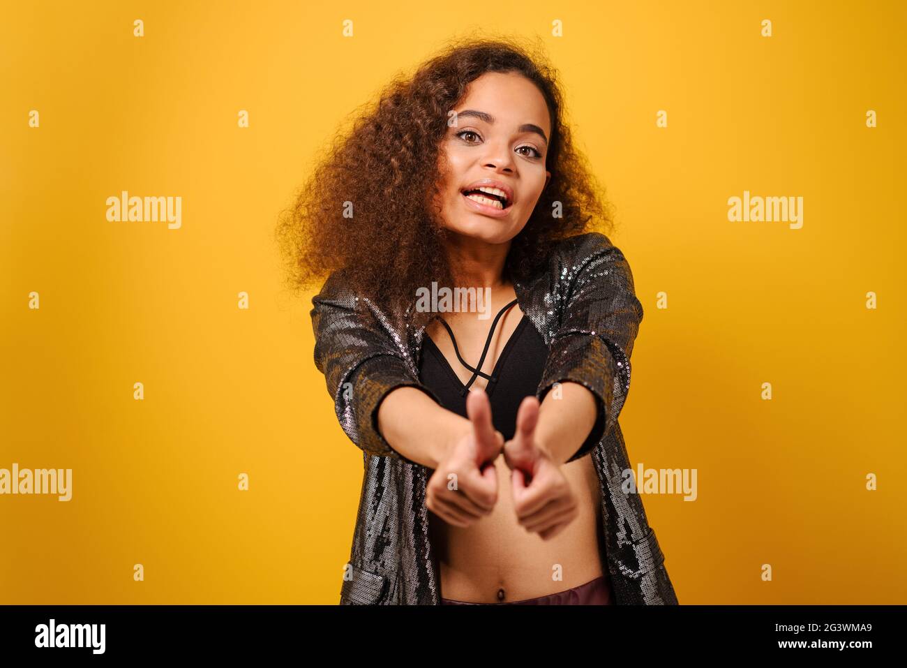 Mani davanti e pollici su felice Afro ragazza americana con bella acconciatura che posa sorriso guardando lato via con la mano su fianchi wea Foto Stock
