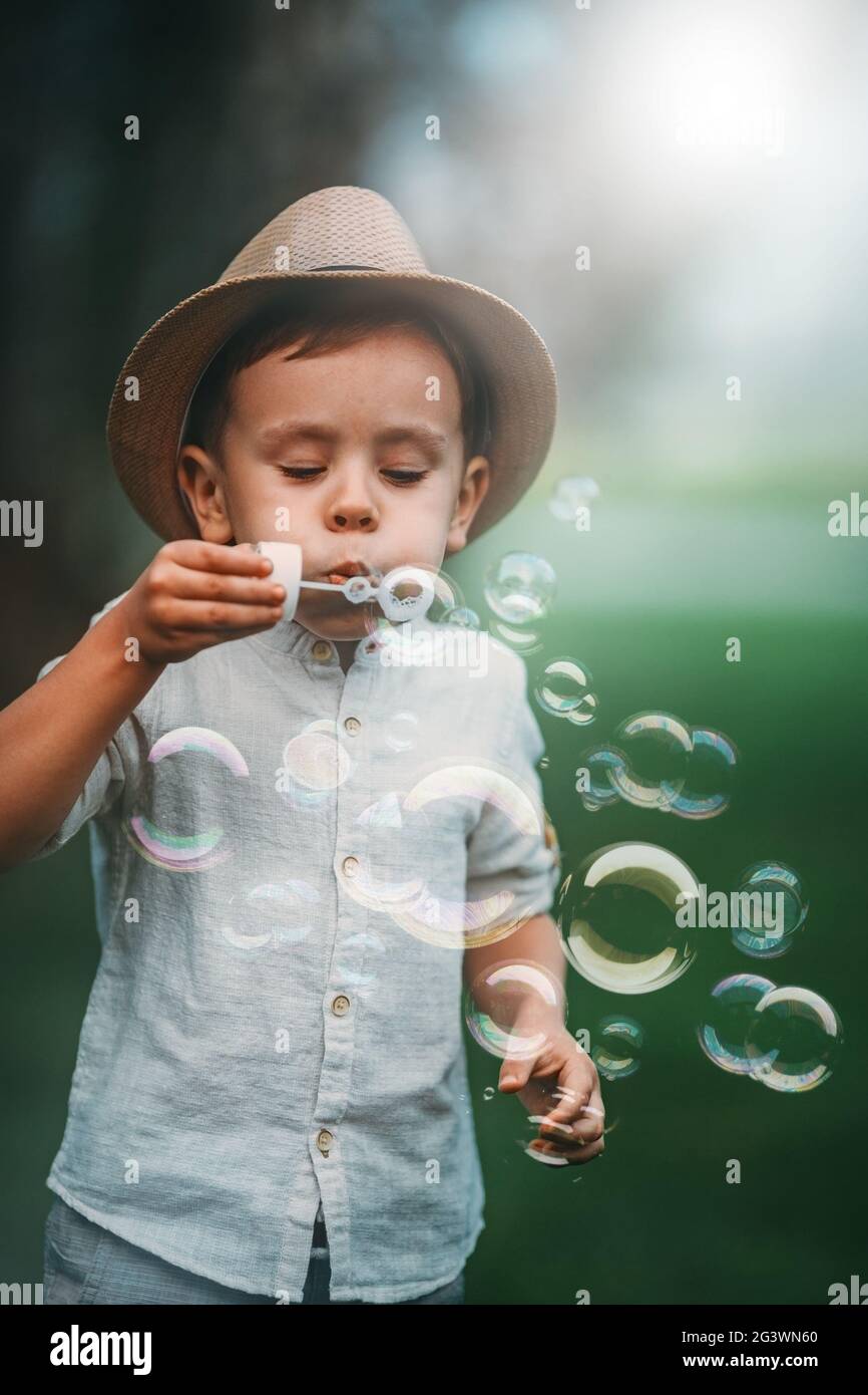 Il bambino soffia diligentemente molte bolle di sapone nel parco. Foto Stock