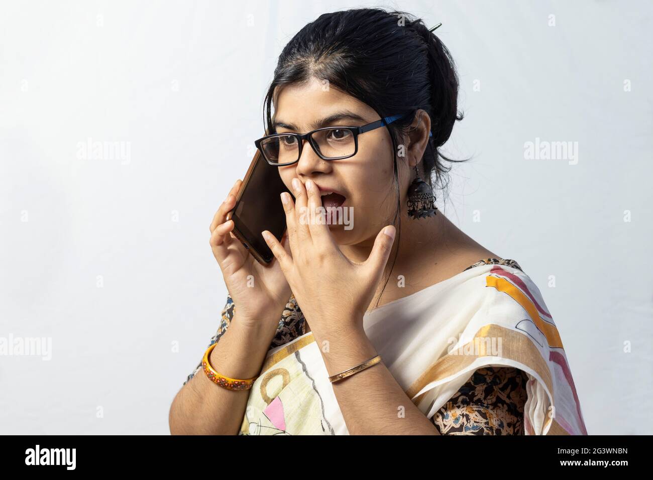 Una bella donna indiana in saree che parla di smartphone con viso sorpreso isolato su sfondo bianco Foto Stock