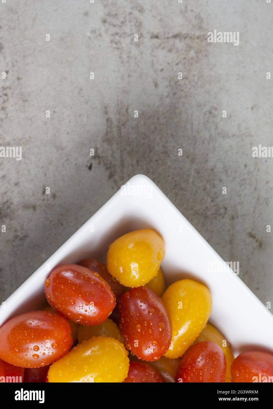 pomodori piccoli rossi e gialli in ciotola quadrata bianca su sfondo grigio. Disposizione piatta. Idea di ricetta Foto Stock