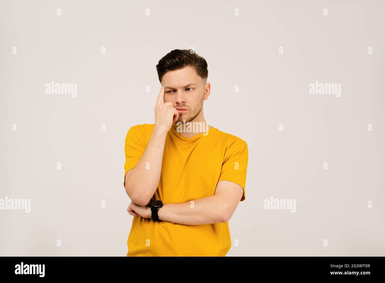 Perso nel pensiero o nel profondo nel pensiero bel giovane uomo ripiegato le mani e tenendo il viso con la mano. Giovane uomo casual in y Foto Stock
