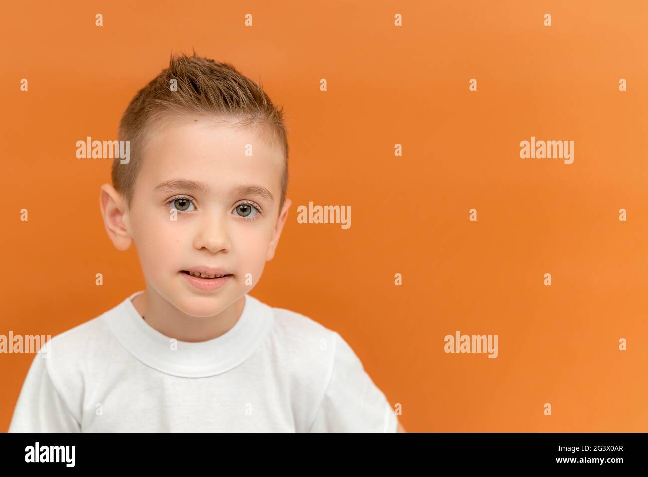 Ritratto di funky carino stupito bambino capretto. Piccolo ragazzo cacasiano con un sorriso simpatico isolato sfondo arancione. Copiare spazio per il testo Foto Stock