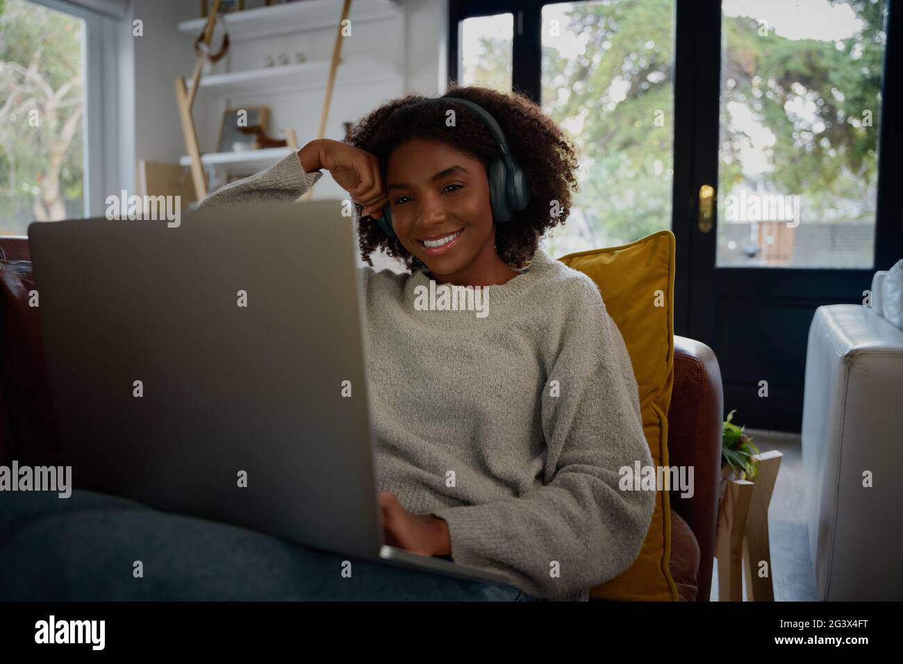 Allegra donna africana che ascolta l'audio in cuffia mentre guardi i video sul computer portatile a casa Foto Stock