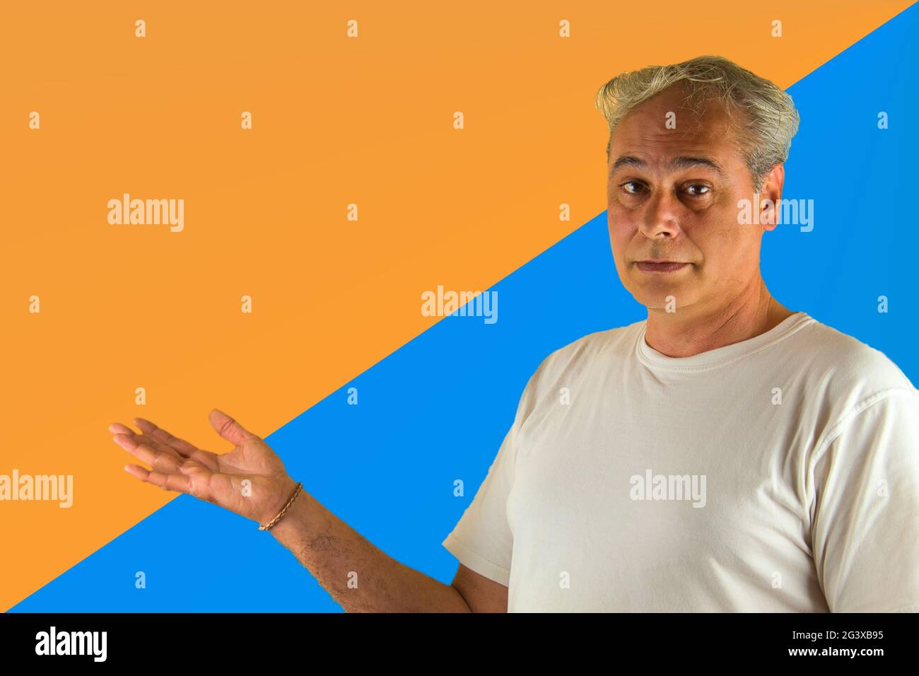 uomo dai capelli grigi che mostra qualcosa con la mano su uno sfondo blu e arancione Foto Stock