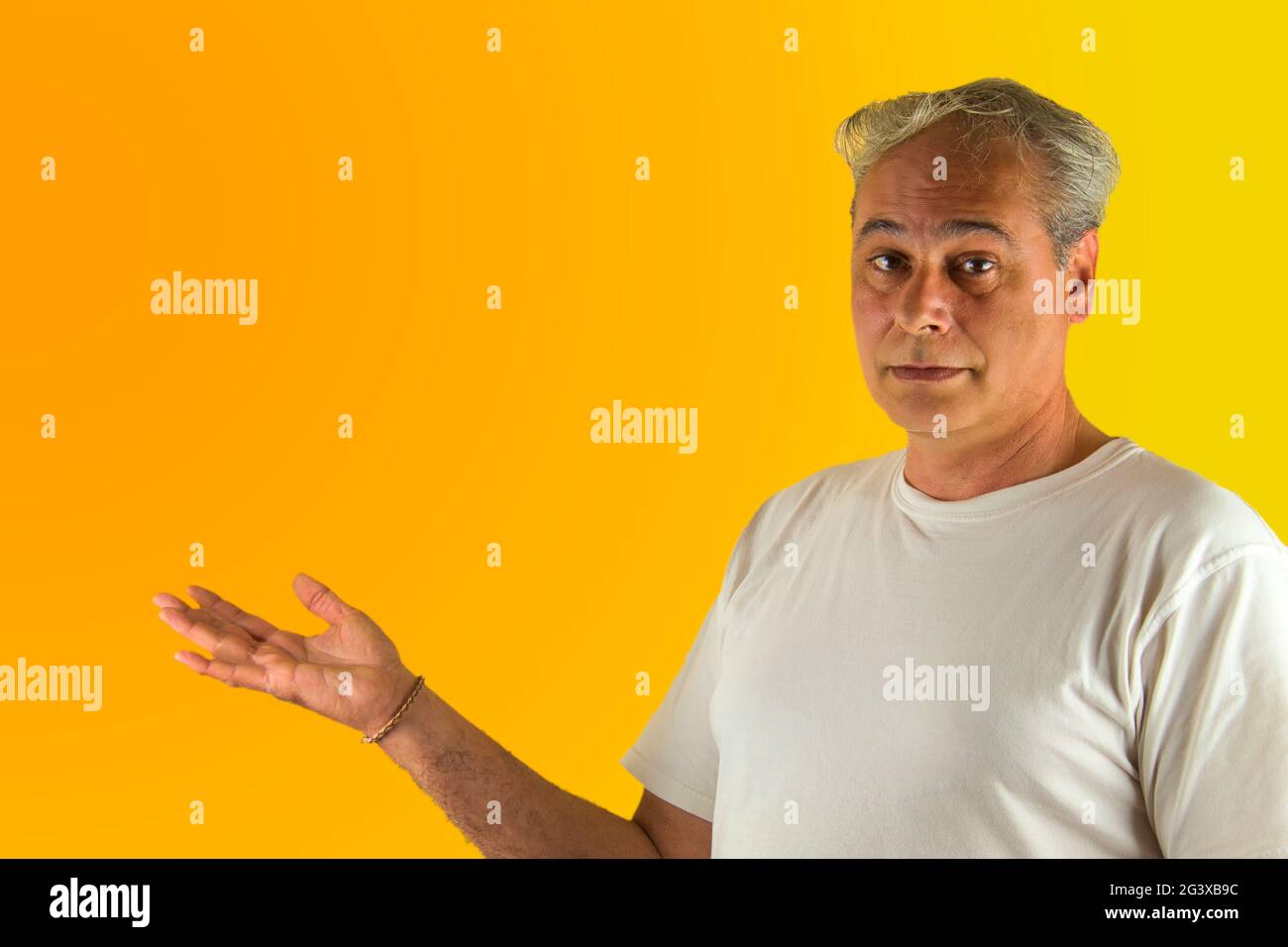 uomo dai capelli grigi che mostra qualcosa con la mano su uno sfondo giallo e arancione Foto Stock