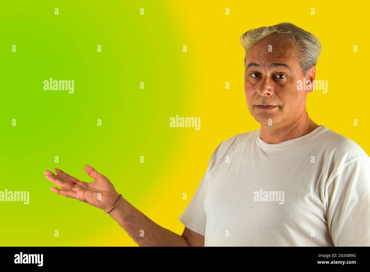 uomo dai capelli grigi che mostra qualcosa con la mano su uno sfondo verde e giallo Foto Stock