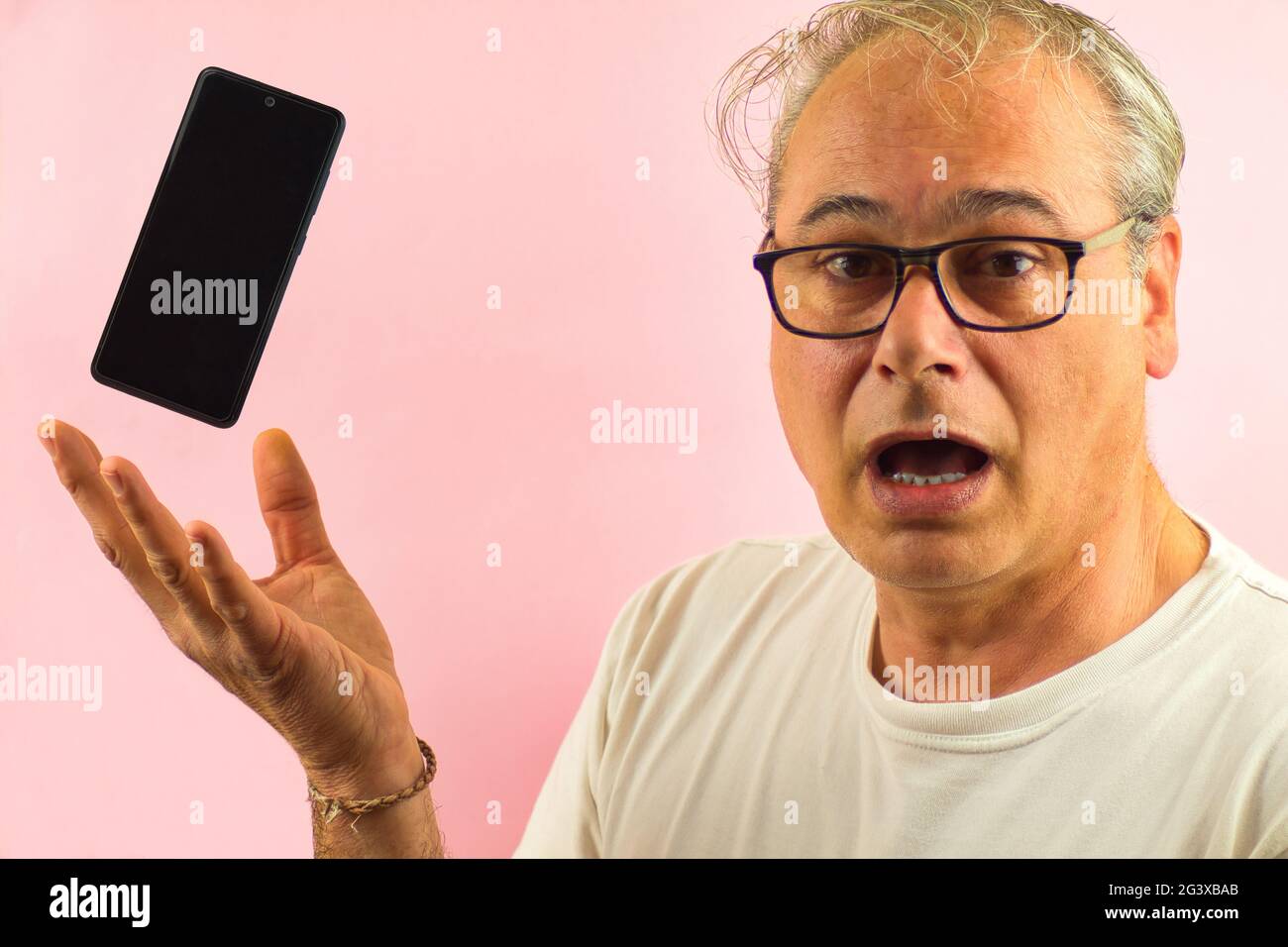 l'uomo maturo con gli occhiali e i capelli grigi mostra sorpreso un mobil con la mano estensibile su sfondo rosa Foto Stock