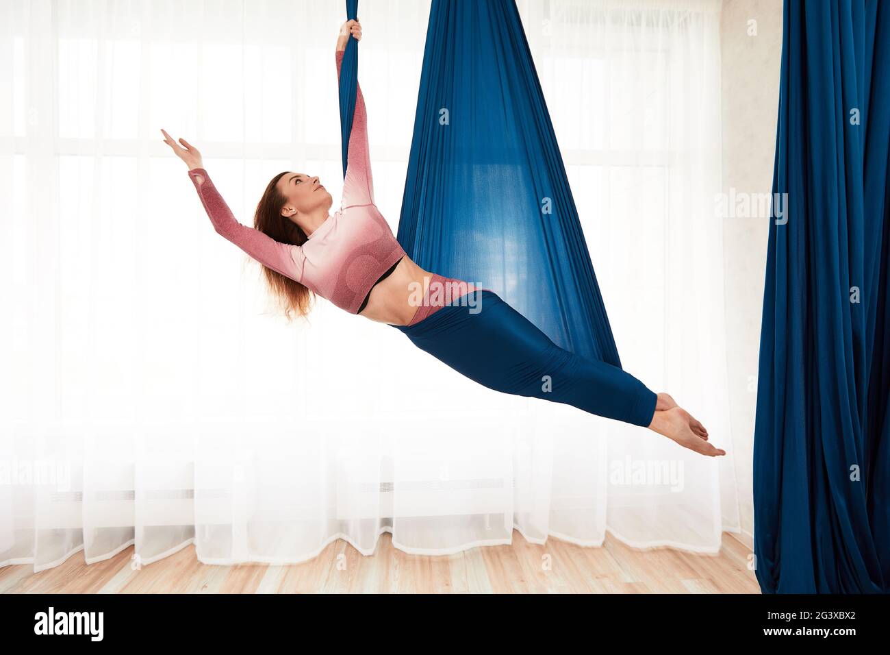 La ragazza è impegnata in yoga aereo in una bella posa in un amaca contro  una grande finestra, una donna sta facendo aerobica antigravitazionale in  un amaca Foto stock - Alamy