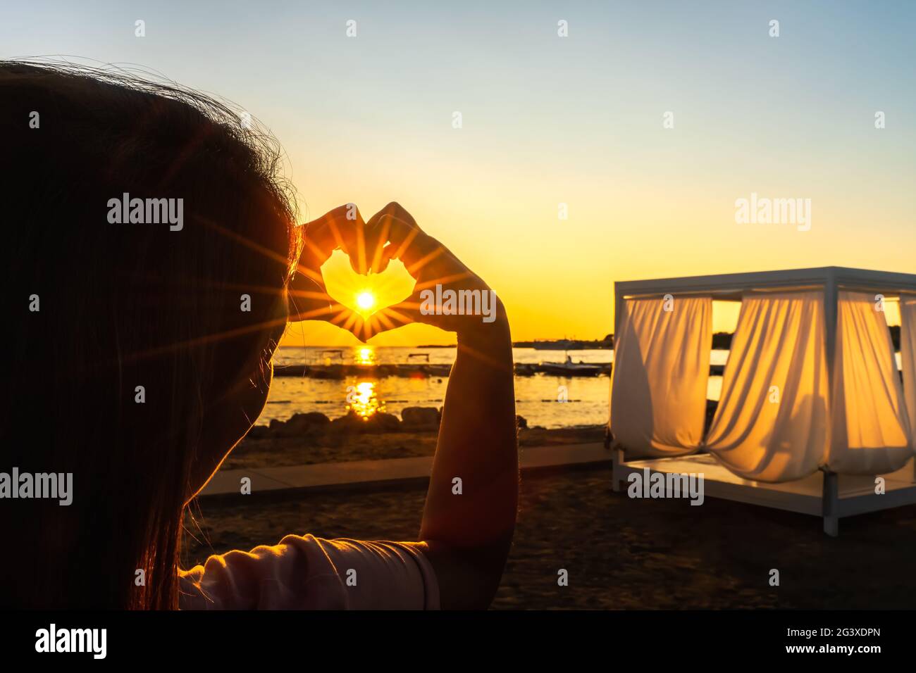 Donna che mostra con le mani cuore strega trogolo brilla Sunstar con i raggi del sole, al bel tramonto Foto Stock