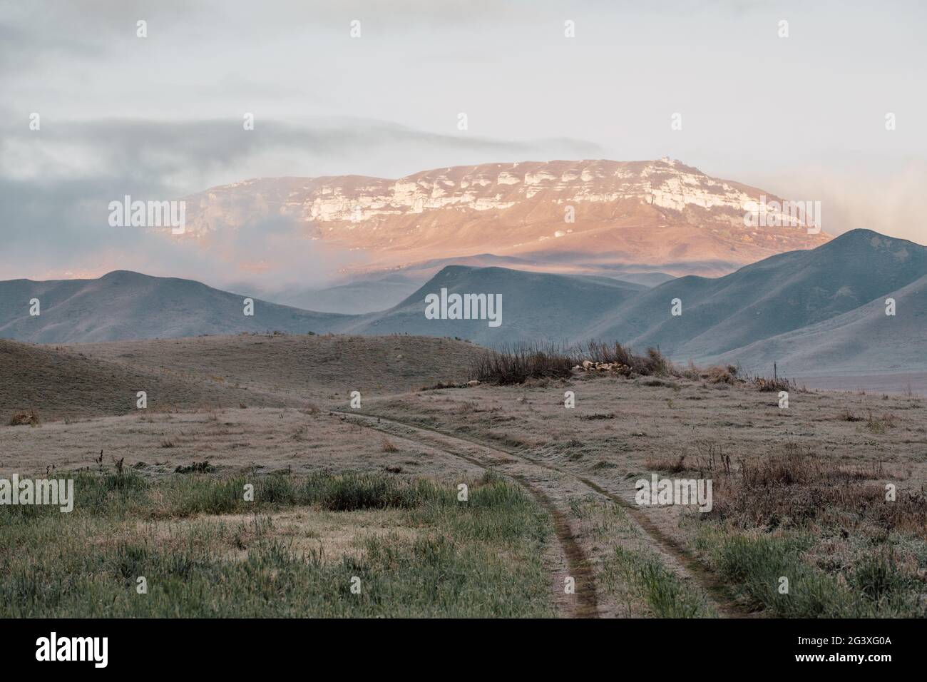 Strada sterrata in campo che va in montagna. Dawn nel campo autunnale. Colline nella foschia mattutina. Erba coperta di rombo autunnale Foto Stock