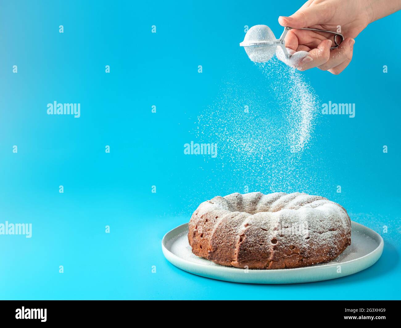 Femmina mano spruzzando zucchero a velo sulla torta a ciambella Foto Stock