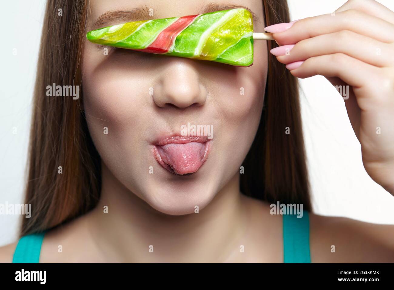 Adolescente ragazza con lollipop fiore in mani chiudere gli occhi e mostrare la lingua. Foto Stock