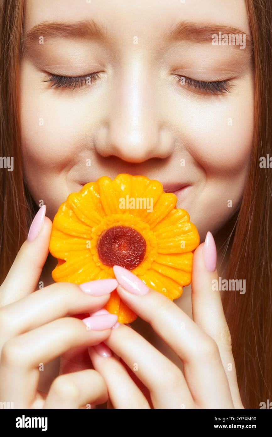 Adolescente ragazza con fiore lollipop in mani chiusura bocca e sorridente. Foto Stock