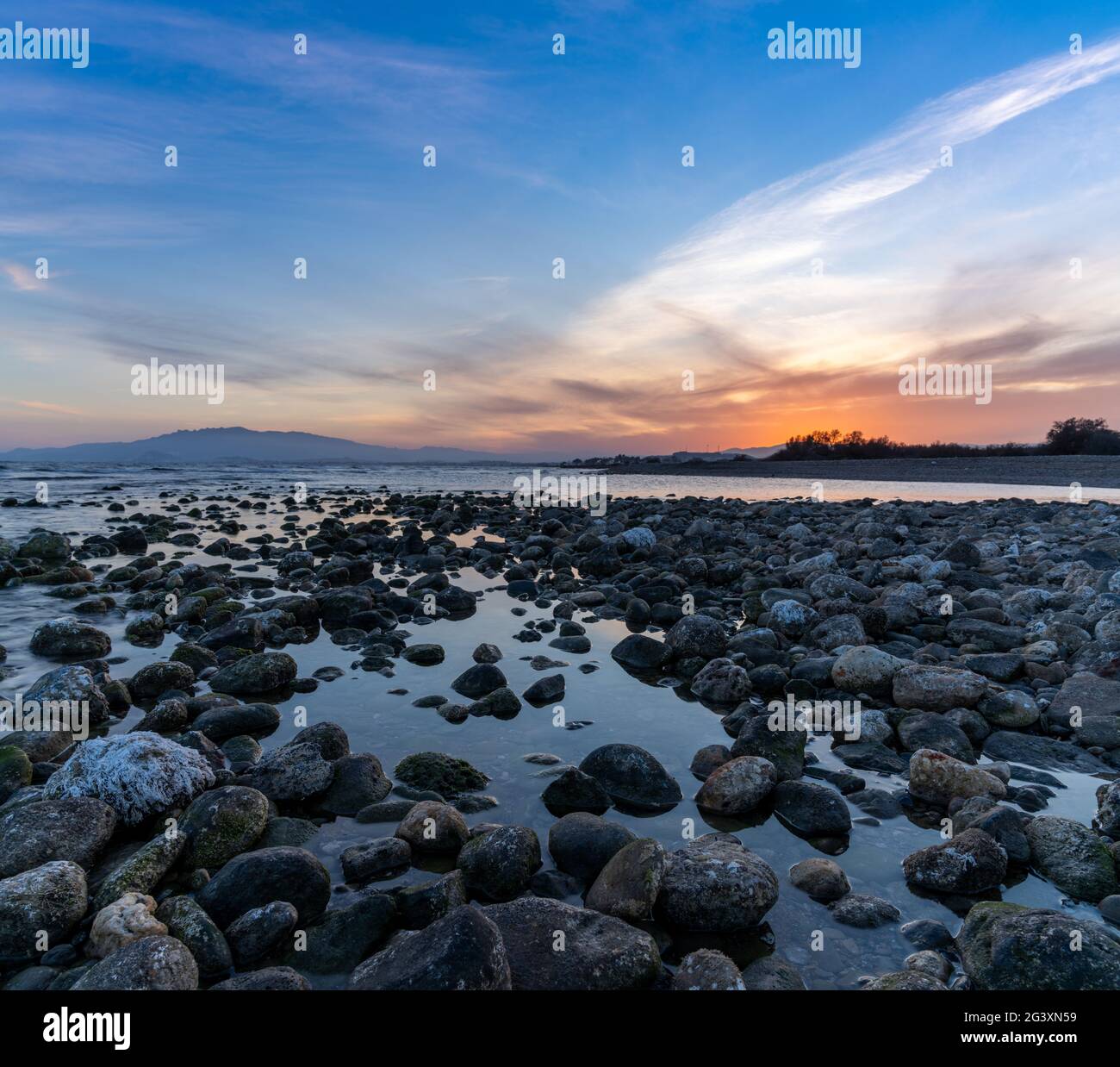 Un colorato tramonto sul Mar Mediterraneo in Almeria con rocce e piscine di marea in primo piano Foto Stock