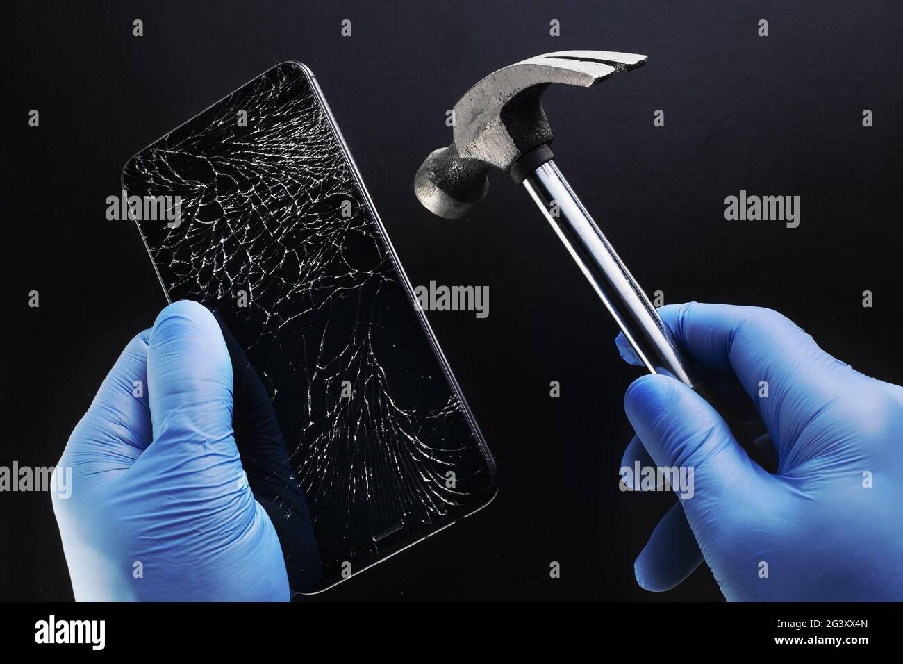 Riparare il telefono in modo irregolare. Uno smartphone con un display rotto e un martello nelle mani di un maestro. Foto Stock