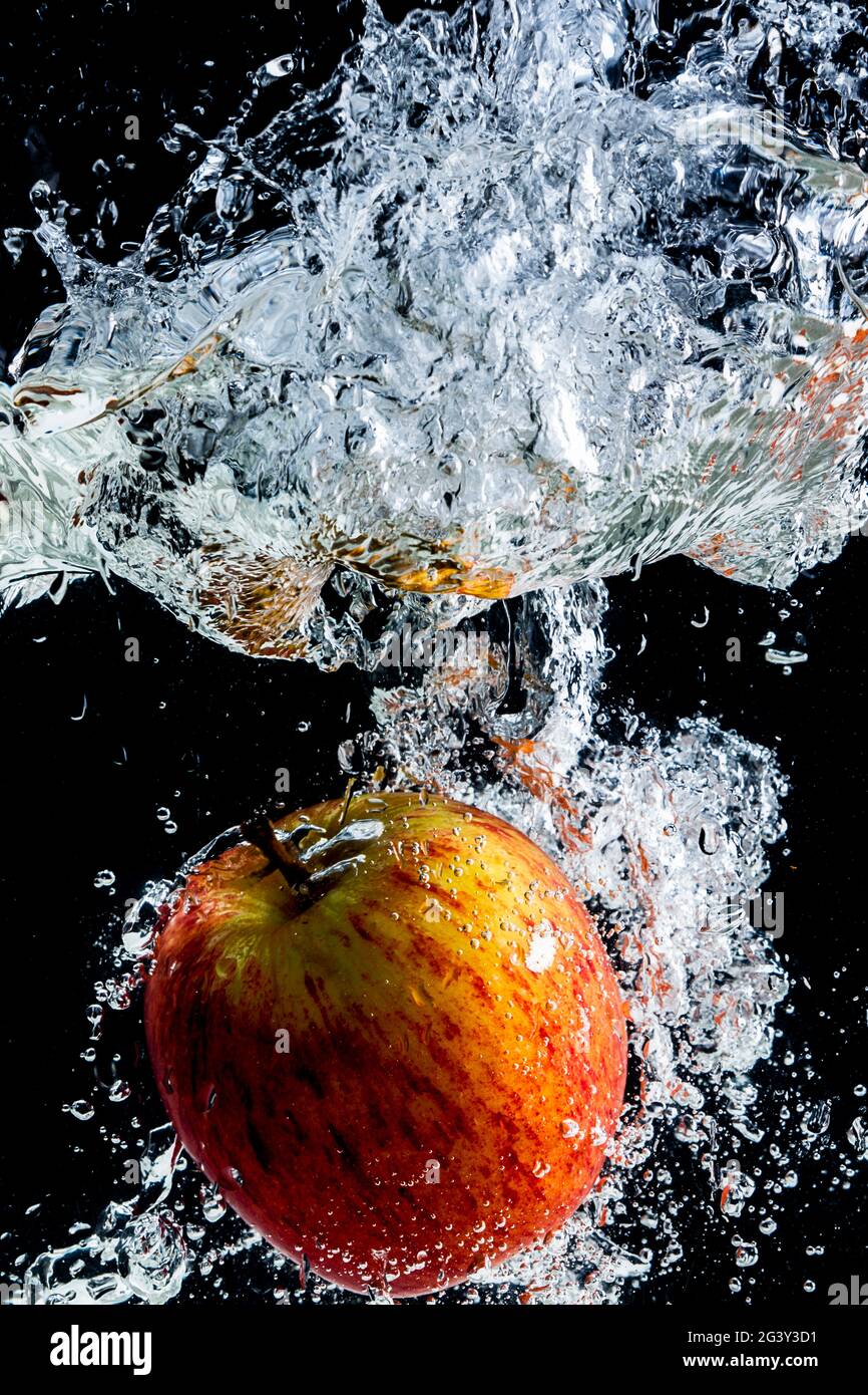 mela rossa gettata in acqua con spruzzi e sfondo nero. Foto Stock