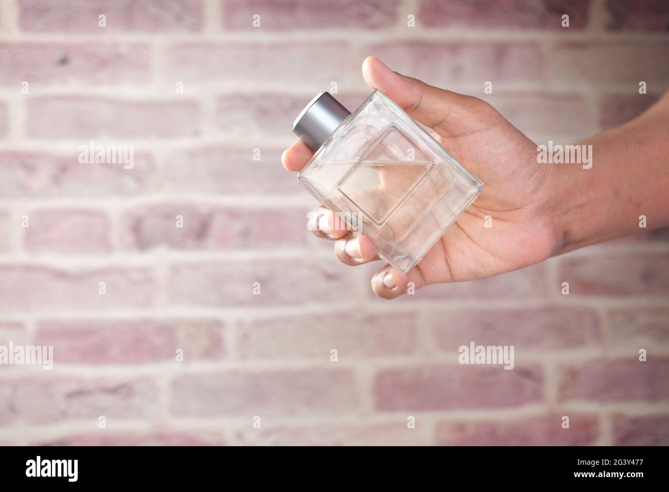 tenere il profumo mano contro sfondo mattone Foto Stock