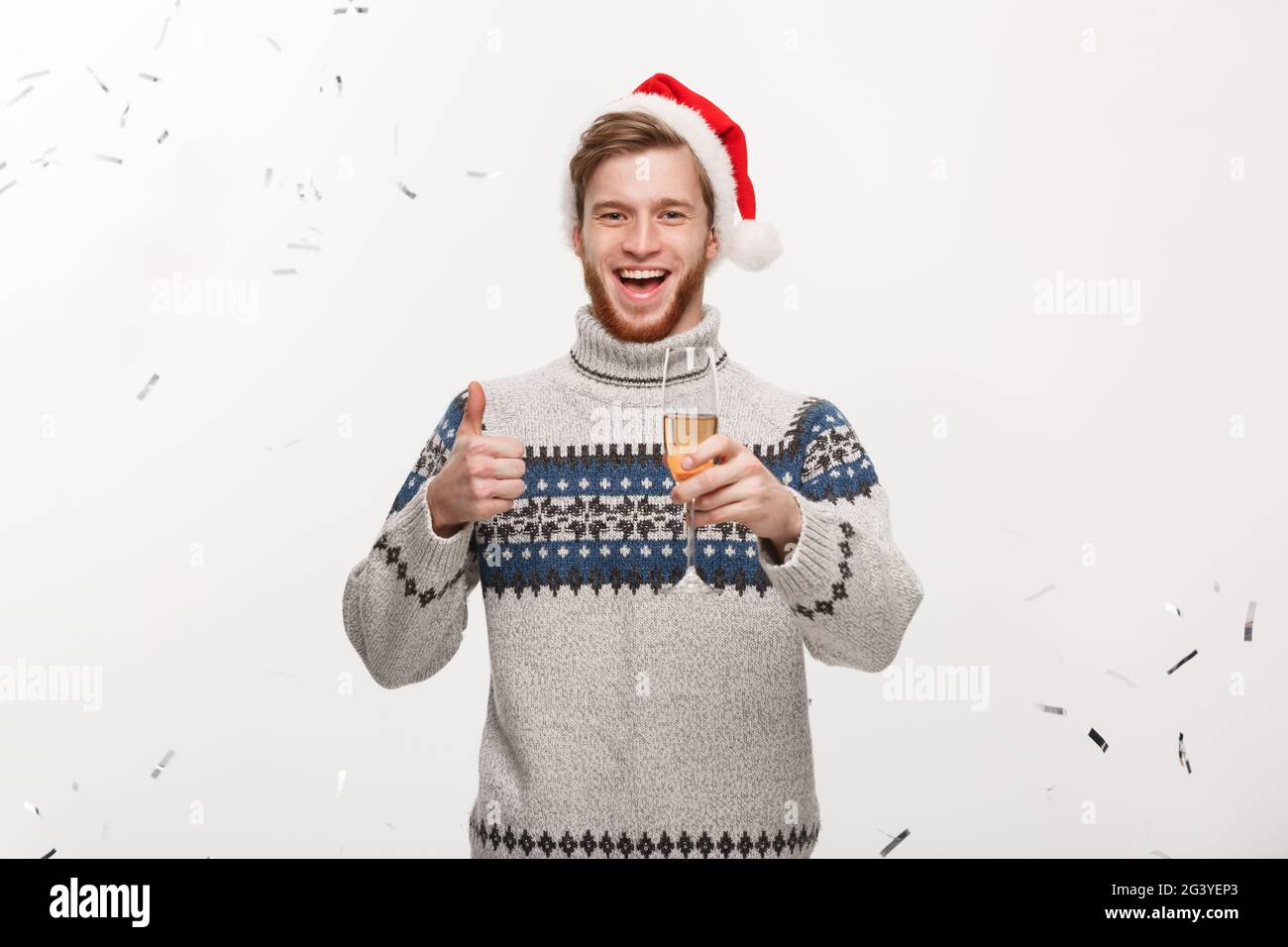 Chirstmas Concept - giovane e felice barba caucasica con bicchiere di champagne con sfondo confetti che festeggia per Natale d Foto Stock