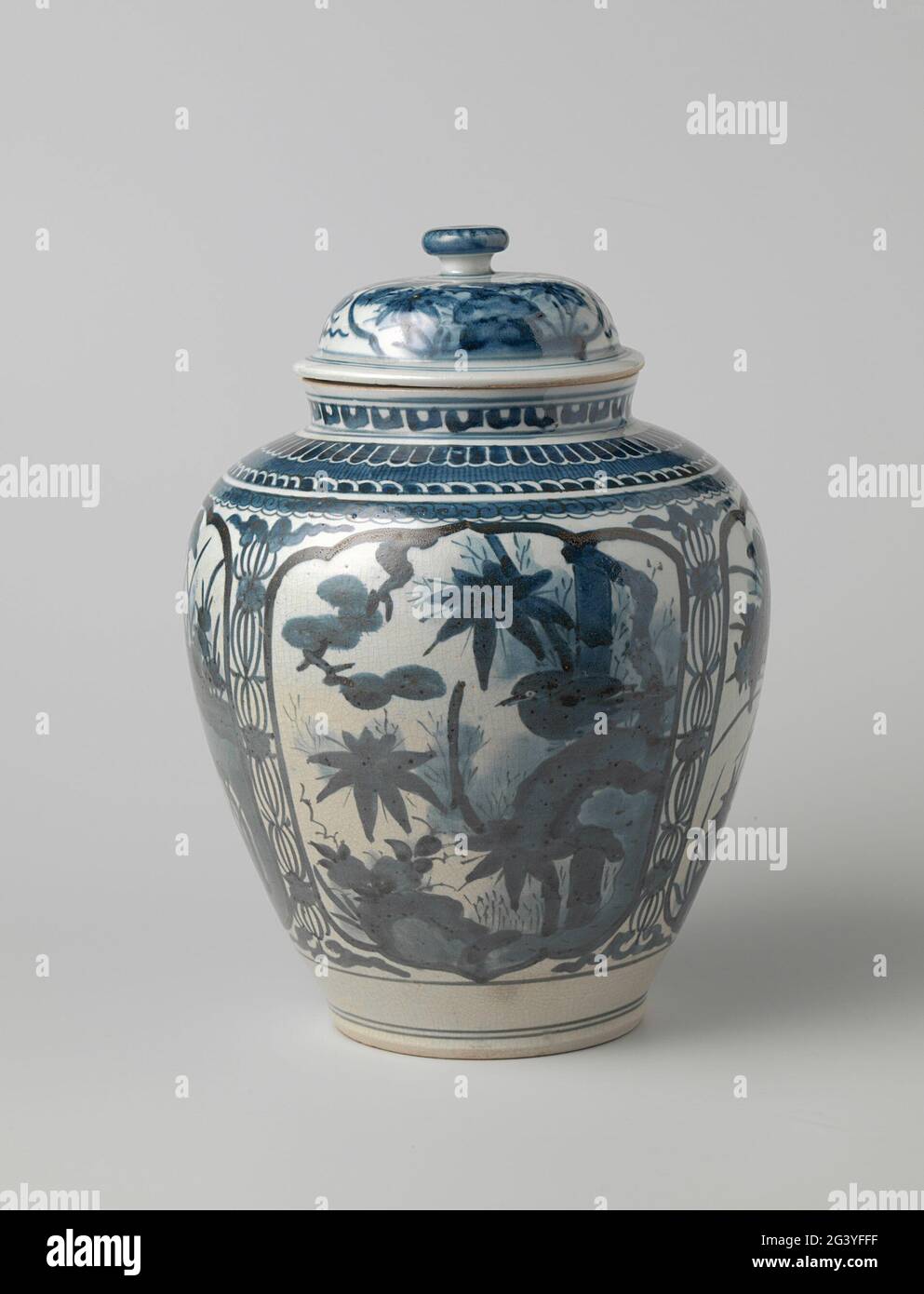 Vaso ovoide coperto con piante in fiore in pannelli e bordi ornamentali. Pentola con coperchio in porcellana a forma d'uovo, verniciata in blu scuro. Sul ventre quattro falciate scaloppate con una pianta fiorente a una roccia e negli altri due un uccello su una roccia a una pianta fiorente. Tra le bevande di fiori di carttocco. Una fascia decorativa sulla spalla e sul collo. Smalto della pentola parzialmente spaccato. Blu Bianco. Foto Stock