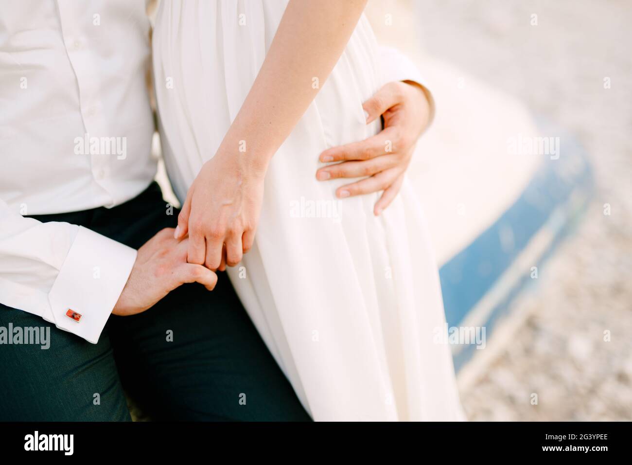 Sposa e sposo si siedono abbracciando e tenendo le mani su una barca capovolta, da vicino Foto Stock