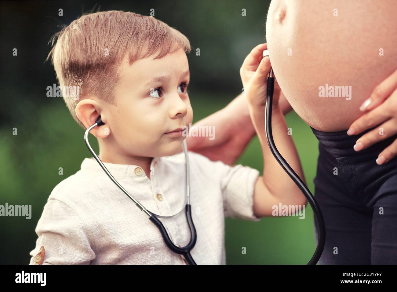 Un ragazzino ascolta con interesse lo stomaco di una madre incinta con uno stetoscopio. Foto Stock