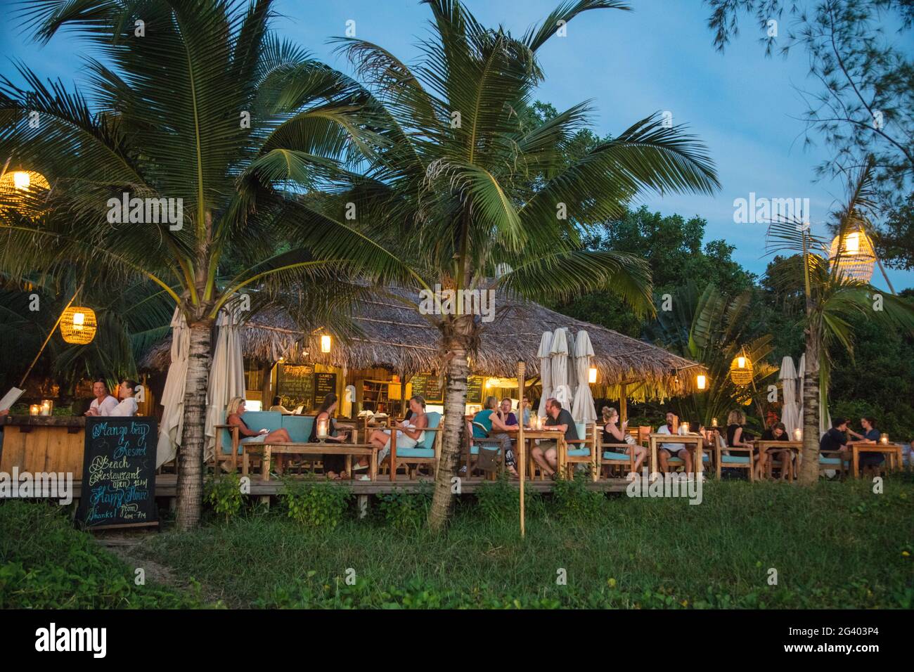 Le persone che godono di bevande nel ristorante e bar del Mango Bay Resort sulla spiaggia di Ong Lang al tramonto, Ong Lang, Phu Quoc Island, Kien Giang, Vietnam, Come Foto Stock