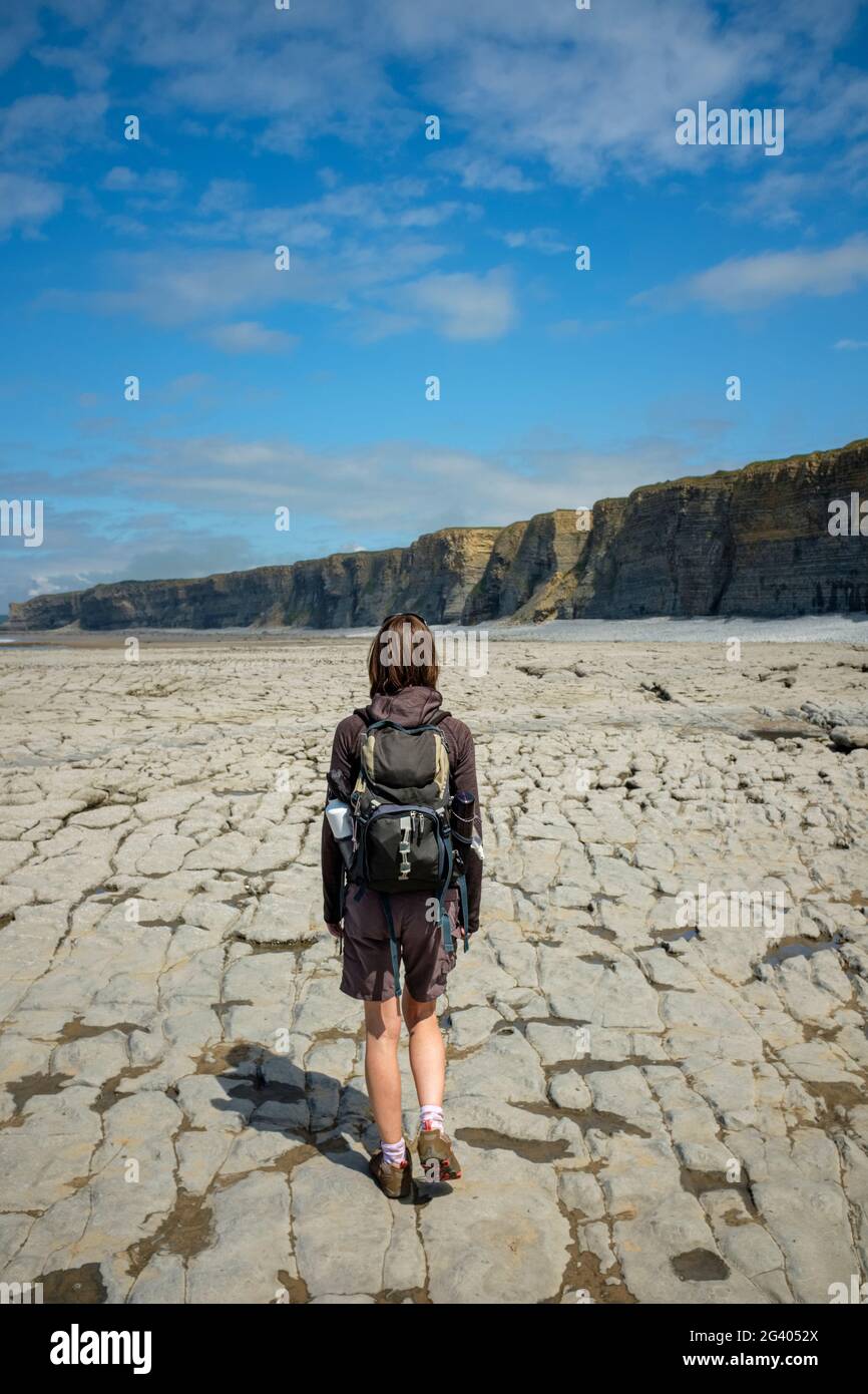 Donna che cammina lungo una costa rocciosa a Nash Point, Galles. Foto Stock