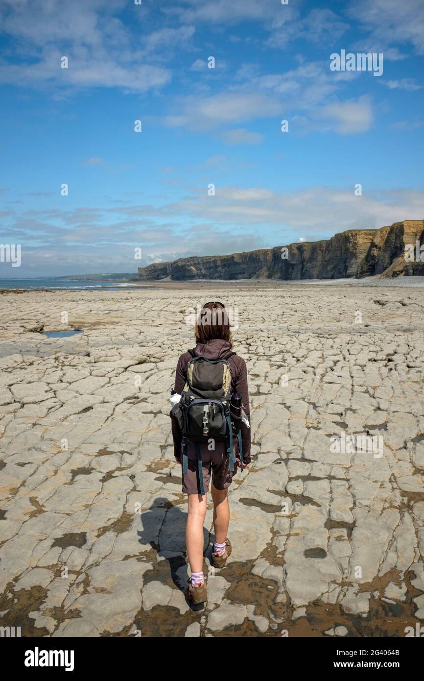 Donna che cammina lungo una costa rocciosa a Nash Point, Galles. Foto Stock