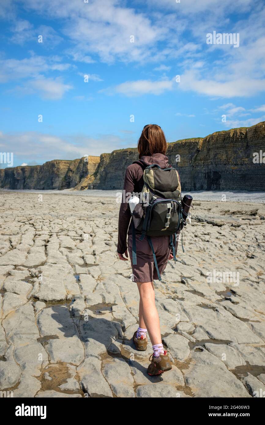 Donna che cammina lungo una costa rocciosa a Nash Point, Galles. Foto Stock