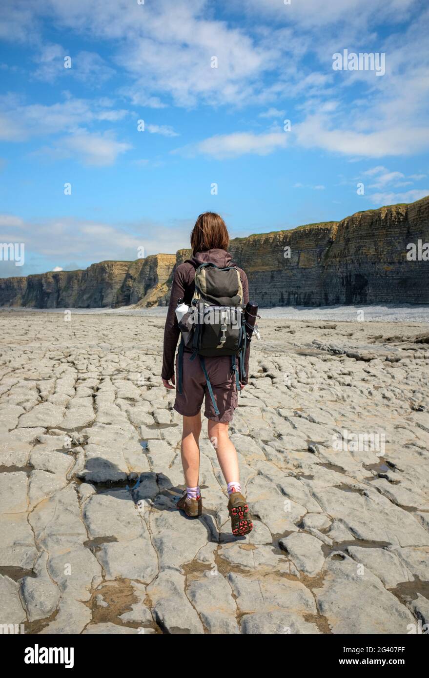 Donna che cammina lungo una costa rocciosa a Nash Point, Galles. Foto Stock