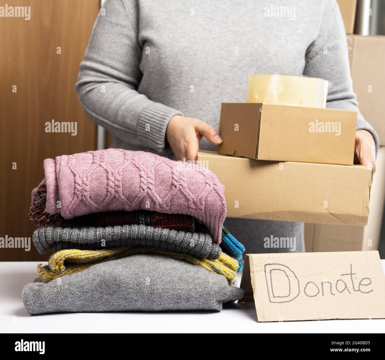 Donna in un maglione grigio sta imballando i vestiti in una scatola, il concetto di assistenza e di volontariato Foto Stock