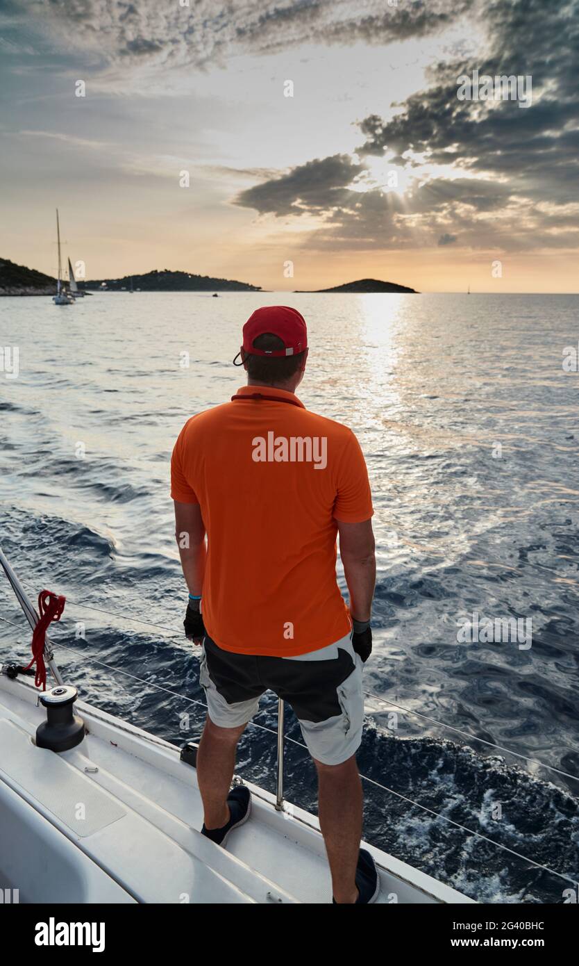 Il partecipante di una regata di vela è sul bordo della barca, gode di una vittoria e un tramonto, si sta vestendo in t-shirt Foto Stock Il partecipante di una regata di vela è sul bordo della barca, gode di una vittoria e un tramonto, si sta vestendo in t-shirt Foto Stock