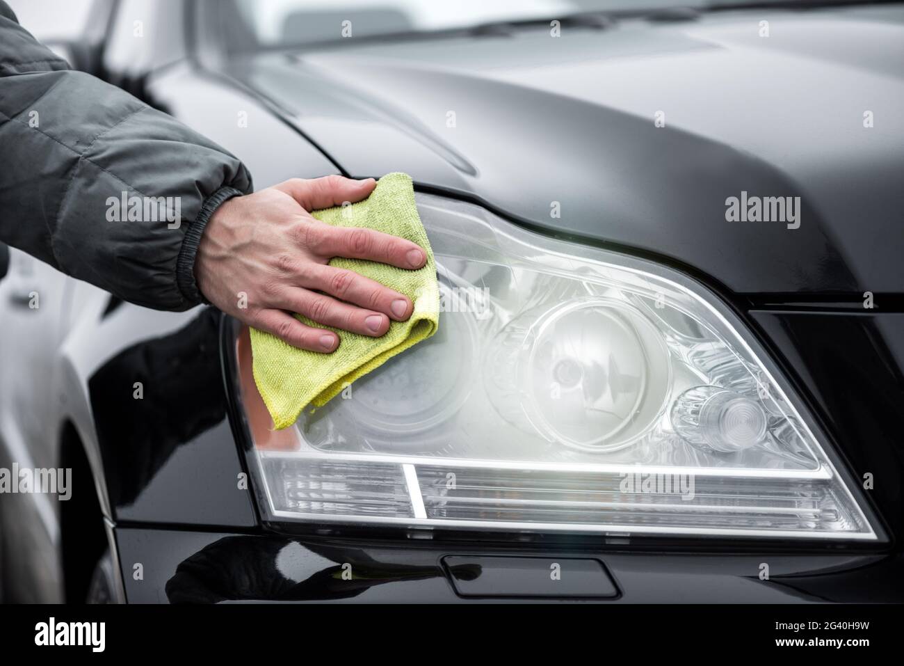 Un uomo che pulisce i fari anteriori della vettura con panno in microfibra, concetto di dettagli della vettura. Foto Stock