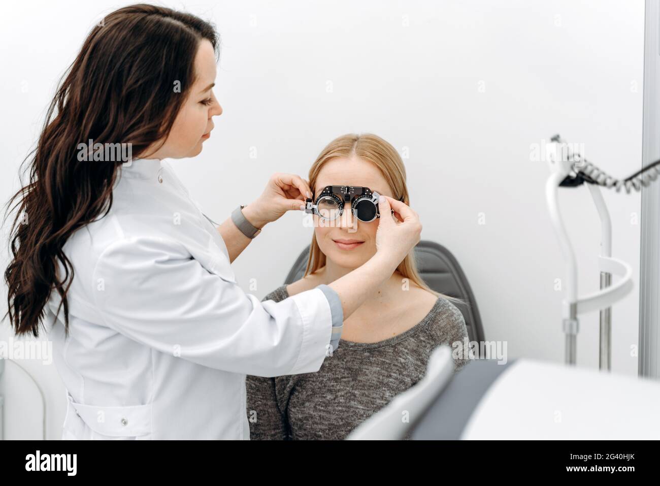 Dispositivo di regolazione del medico. Ragazza buona-osservante positiva che si prepara per misurare i suoi bulbi oculari durante l'appuntamento con l'oftalmologo. Foto Stock