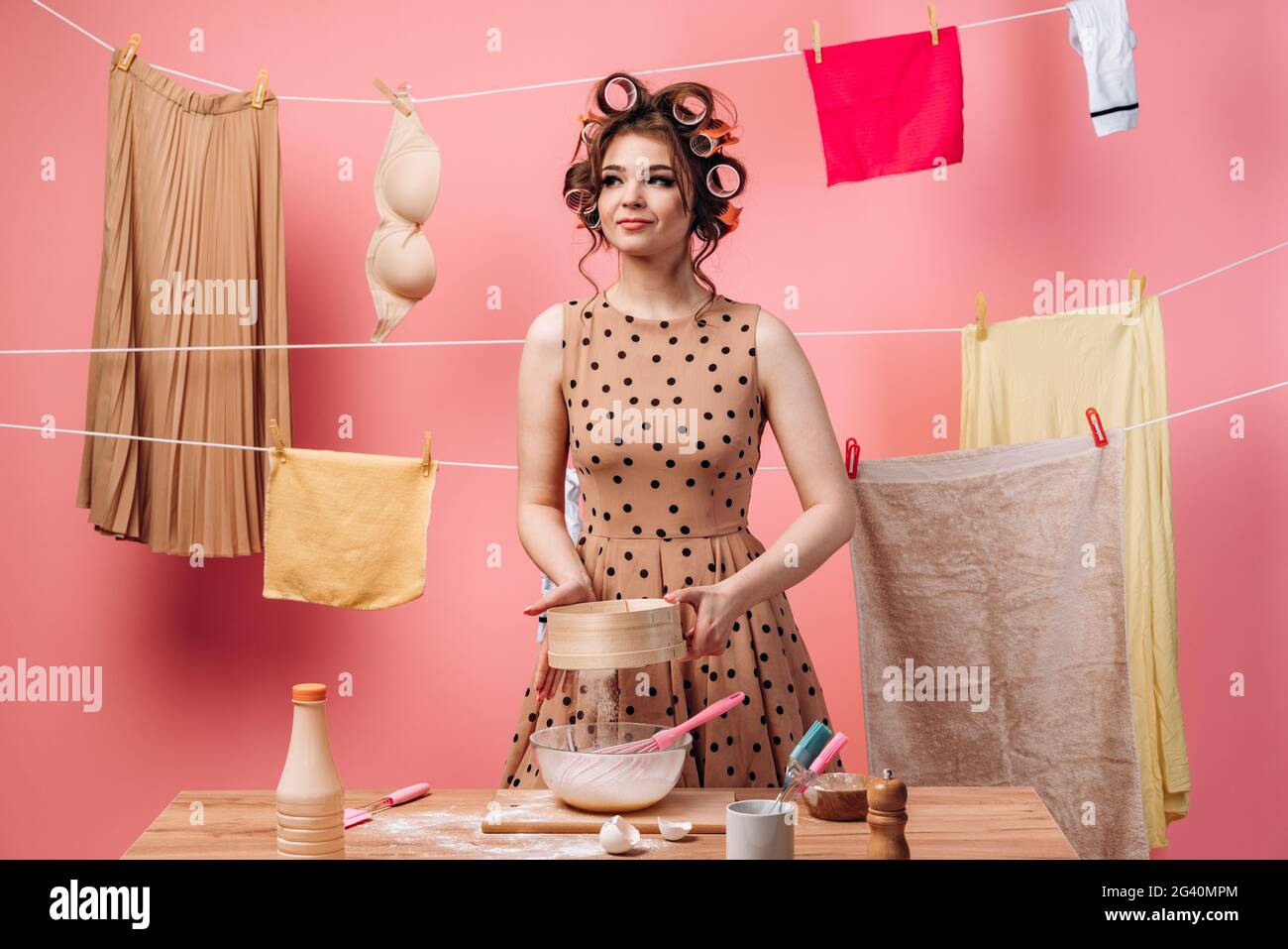 Donna prepara il cibo, setola la farina attraverso un setaccio. Bella casalinga è occupato con le faccende domestiche su uno sfondo rosa. Foto Stock