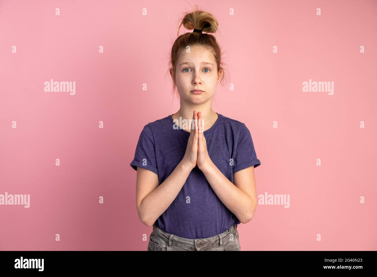 Bambina che prega su sfondo rosa. I bambini premono insieme le mani sul petto. Spiritualità di fede e concetto di religione. Foto Stock