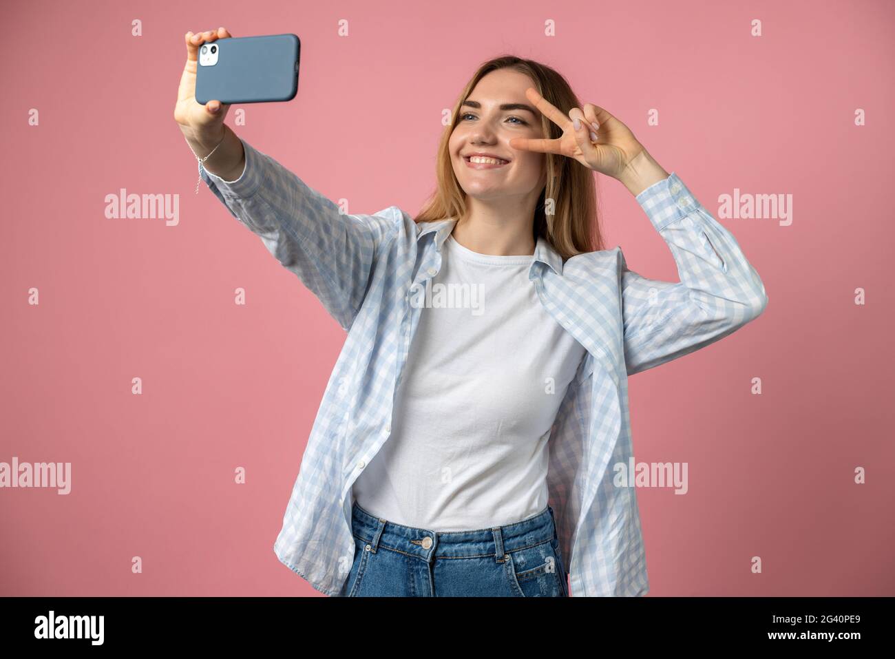 Ragazza di buon umore fa un selfie sul telefono su uno sfondo di una parete rosa. Gioiosa giovane ragazza che posa isolata su sfondo rosa. Foto Stock